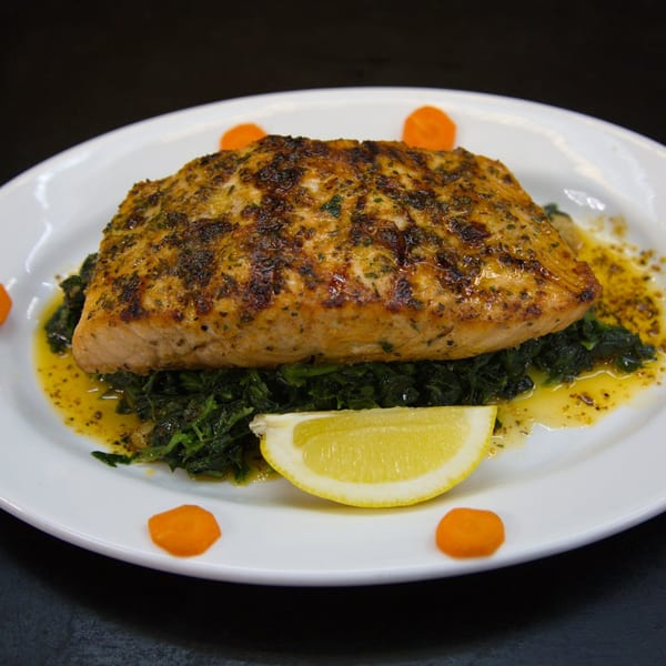 Grilled salmon fillet on a bed of sautéed spinach with a lemon wedge and carrot slices.