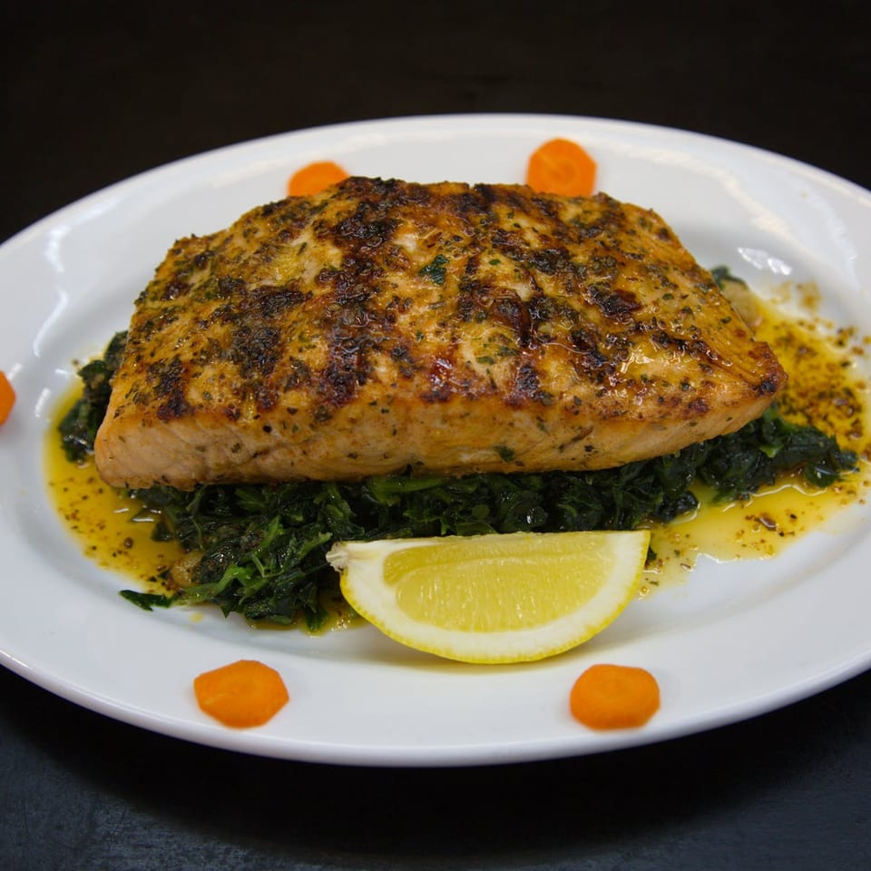 Grilled salmon fillet on a bed of sautéed spinach with a lemon wedge and carrot slices.