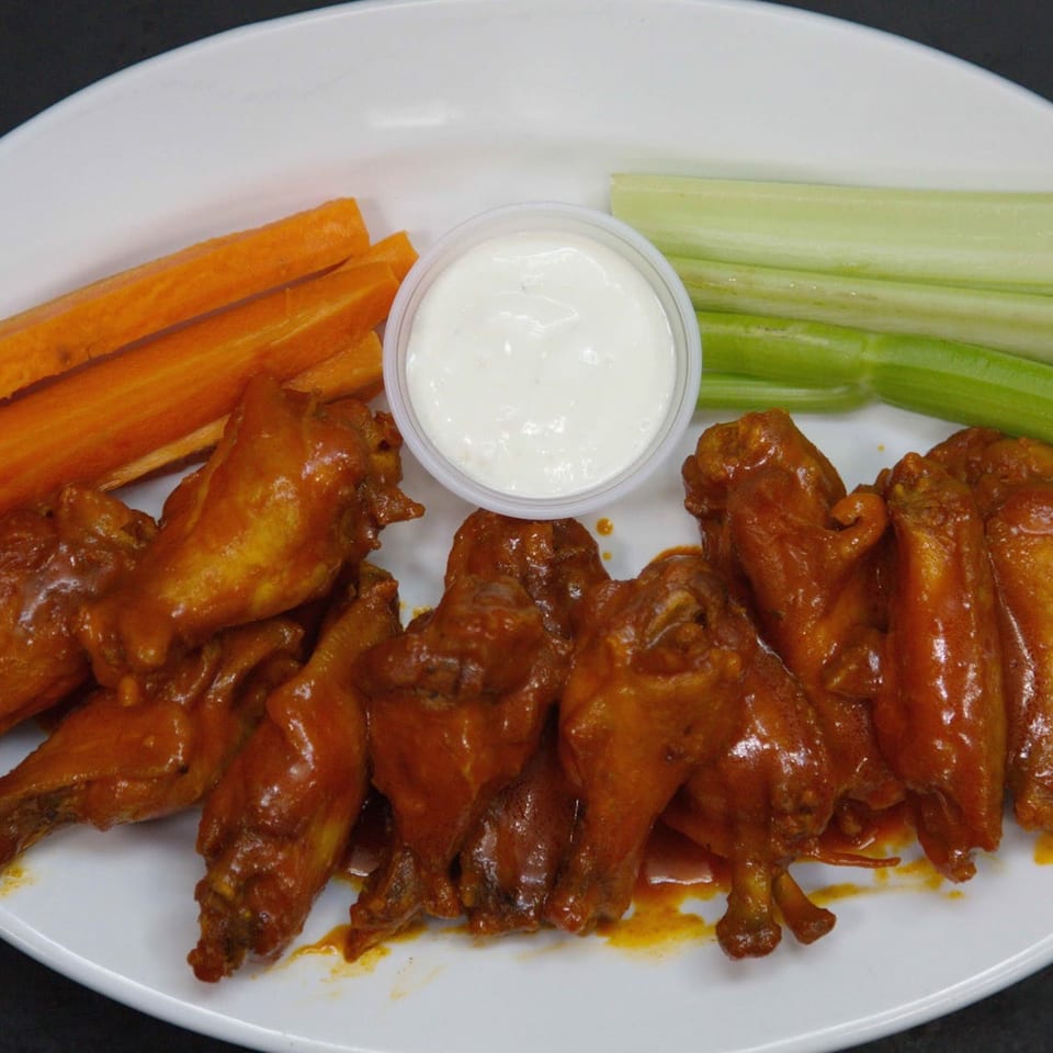 Spicy buffalo wings with carrots, celery, and ranch dressing on a white plate.