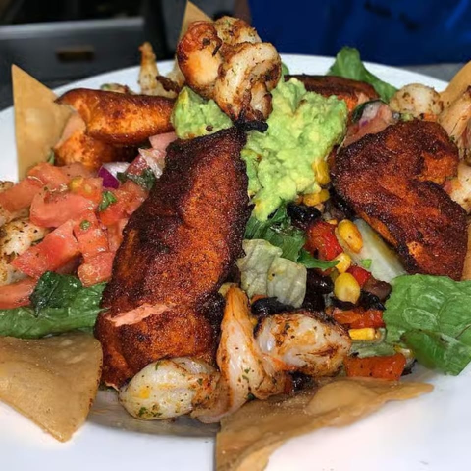 A vibrant salad with grilled chicken, shrimp, guacamole, salsa, corn, and tortilla chips.