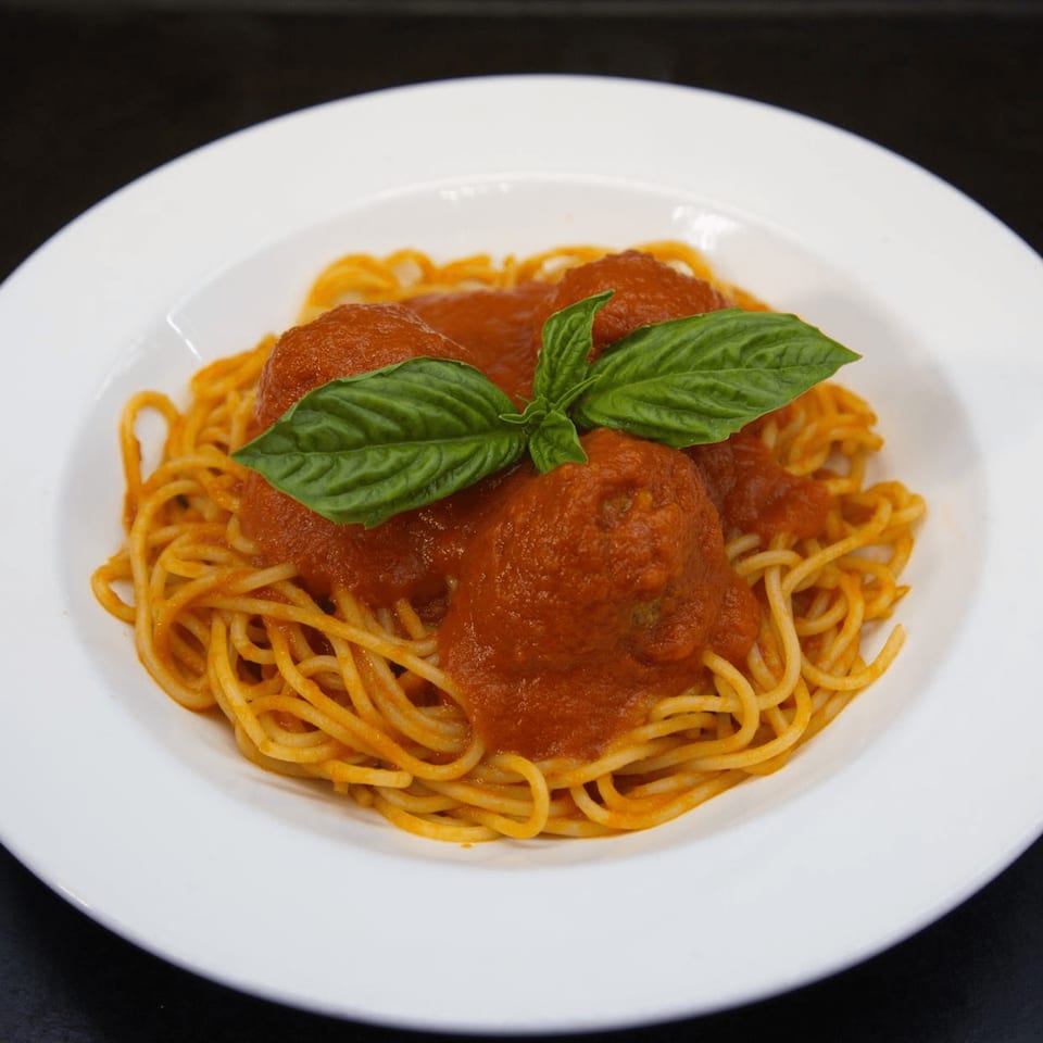 Spaghetti with meatballs and marinara sauce, garnished with fresh basil, on a white plate.