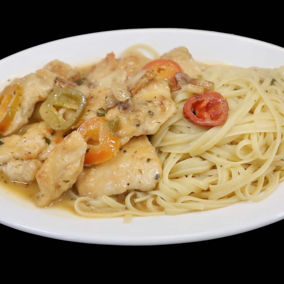 Chicken scaloppine with mushrooms, peppers, and tomatoes, served alongside linguine pasta on a white plate.