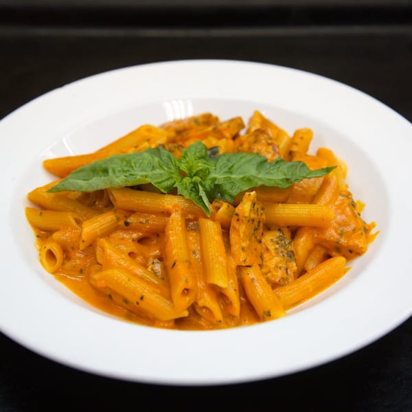 Penne pasta with creamy orange sauce, chicken, and fresh basil in a white bowl.