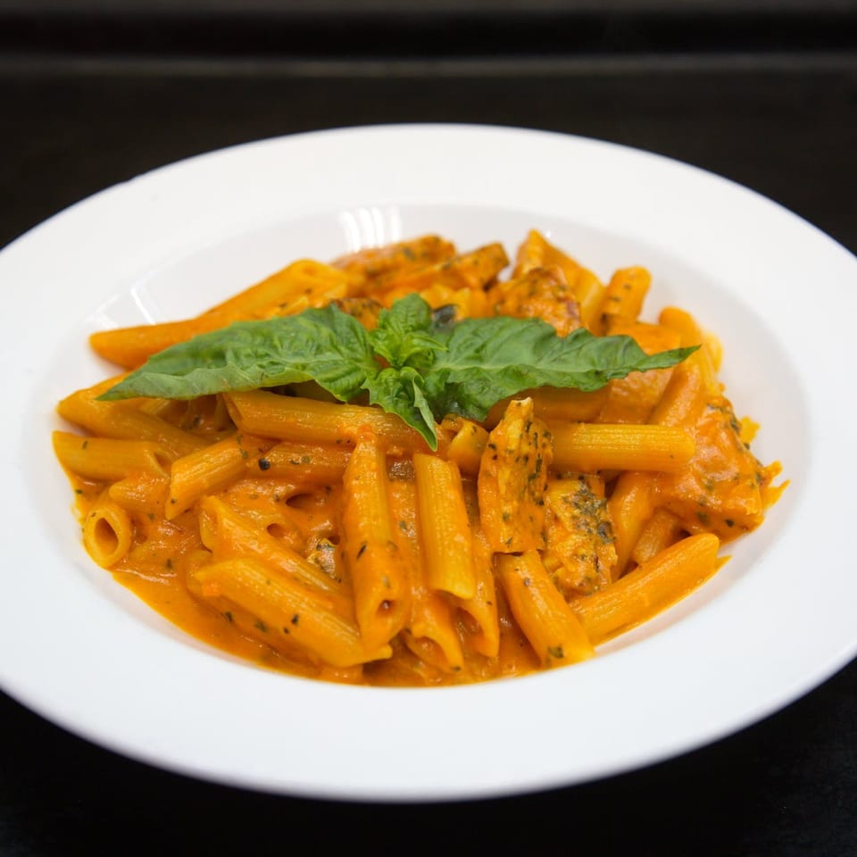 Penne pasta with creamy orange sauce, chicken, and fresh basil in a white bowl.
